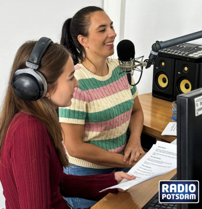 Interview im Radiostudio: Zwei Frauen sitzen vor Mikrofon und Mischpult, eine trägt Kopfhörer und hält ein Manuskript – Aufnahme für Radio Potsdam.