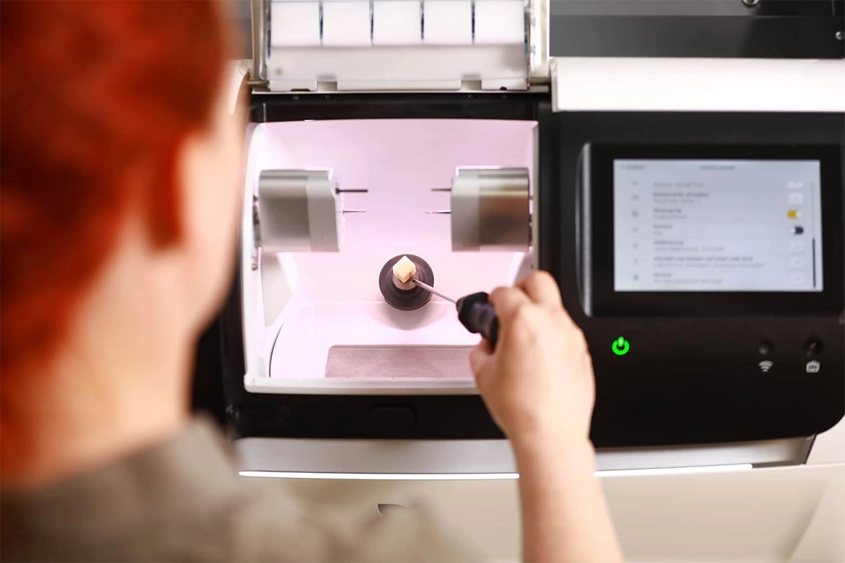 Digitale Zahntechnik im Einsatz – Mitarbeiterin bearbeitet ein Keramik-Element in einer modernen CAD/CAM-Fräsmaschine zur präzisen Herstellung von Zahnersatz.