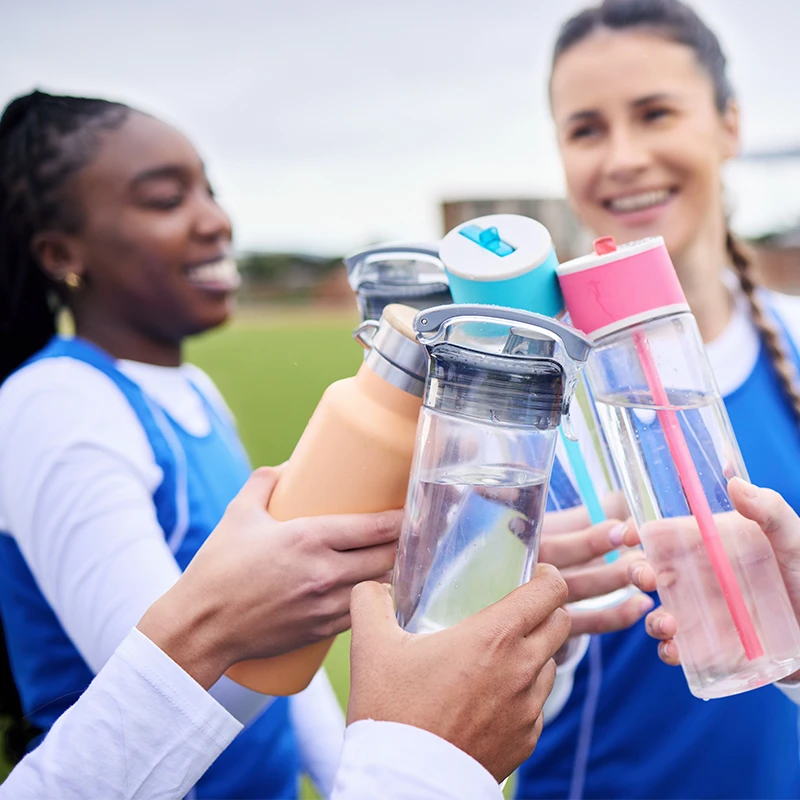 Sportlerinnen stoßen auf dem Spielfeld mit Trinkflaschen an – Symbol für Teamgeist, Gesundheit und ausreichende Flüssigkeitszufuhr beim Training.