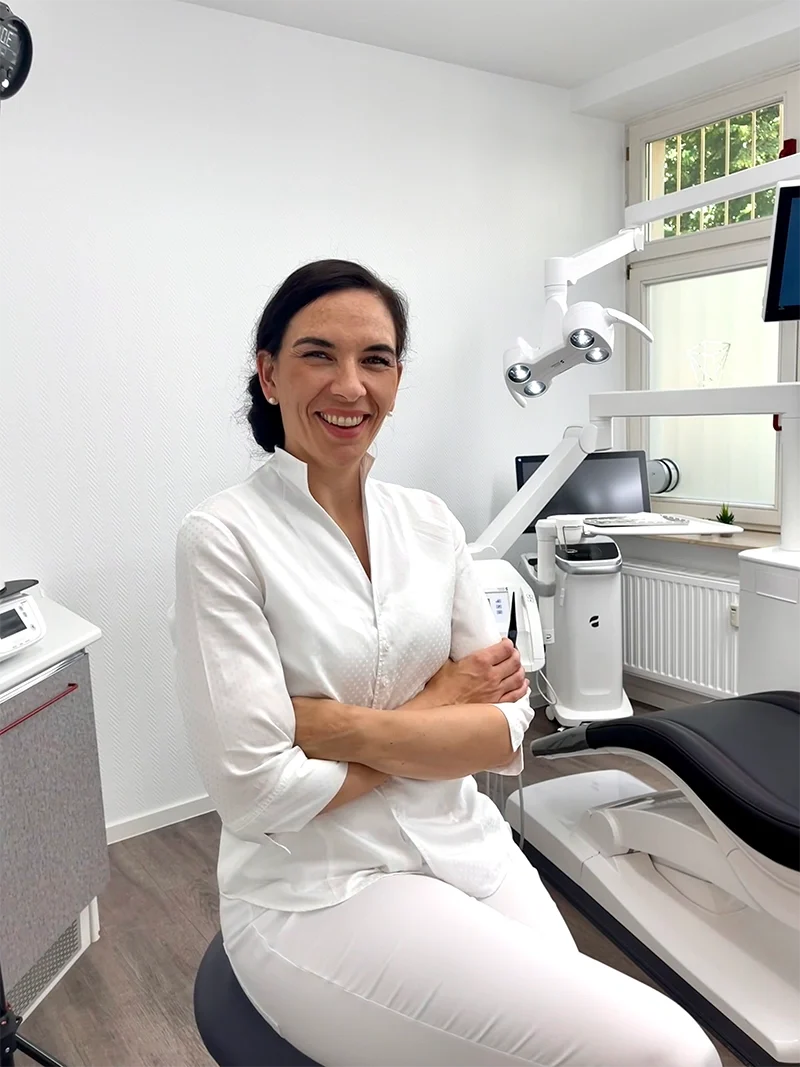 Dr. Szabadi lächelt im modernen Behandlungsraum der Praxis und steht für hochwertige professionelle Zahnpflege und individuelle Betreuung.